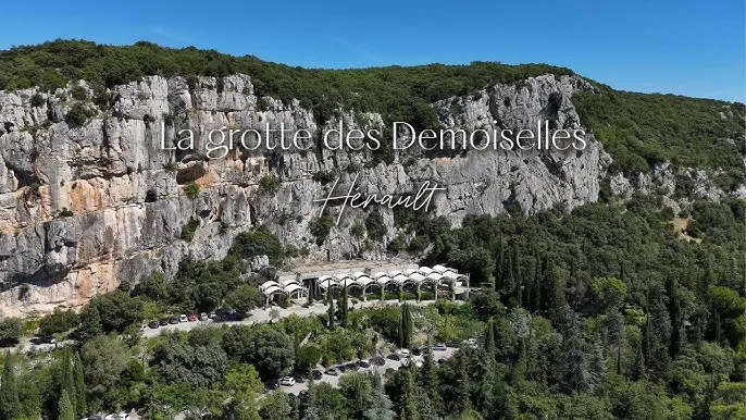 Vue extérieure de la Grotte des Demoiselles dans l'Hérault, entourée de paysages rocheux et de verdure.