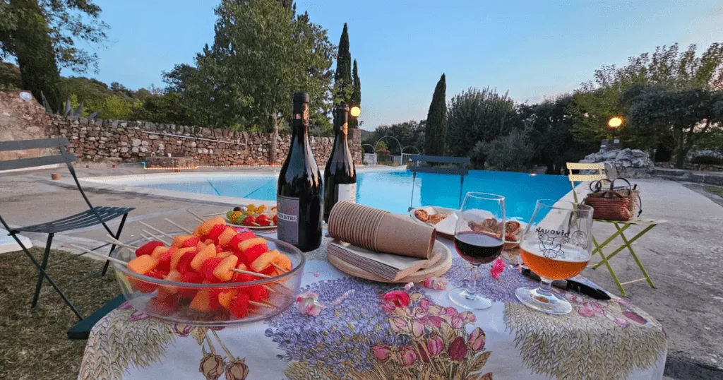 Table dressée en plein air au Camping de La Devèze, avec des vins locaux, des fruits frais et une vue sur les collines environnantes.